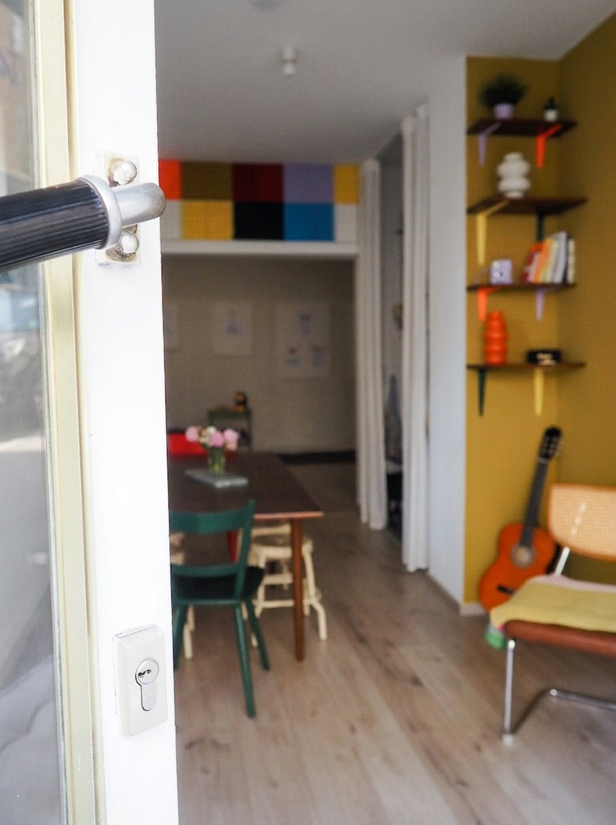 Blick durch die Eingangstür auf ein Farbraster an der Wand und den Aufenthaltsraum